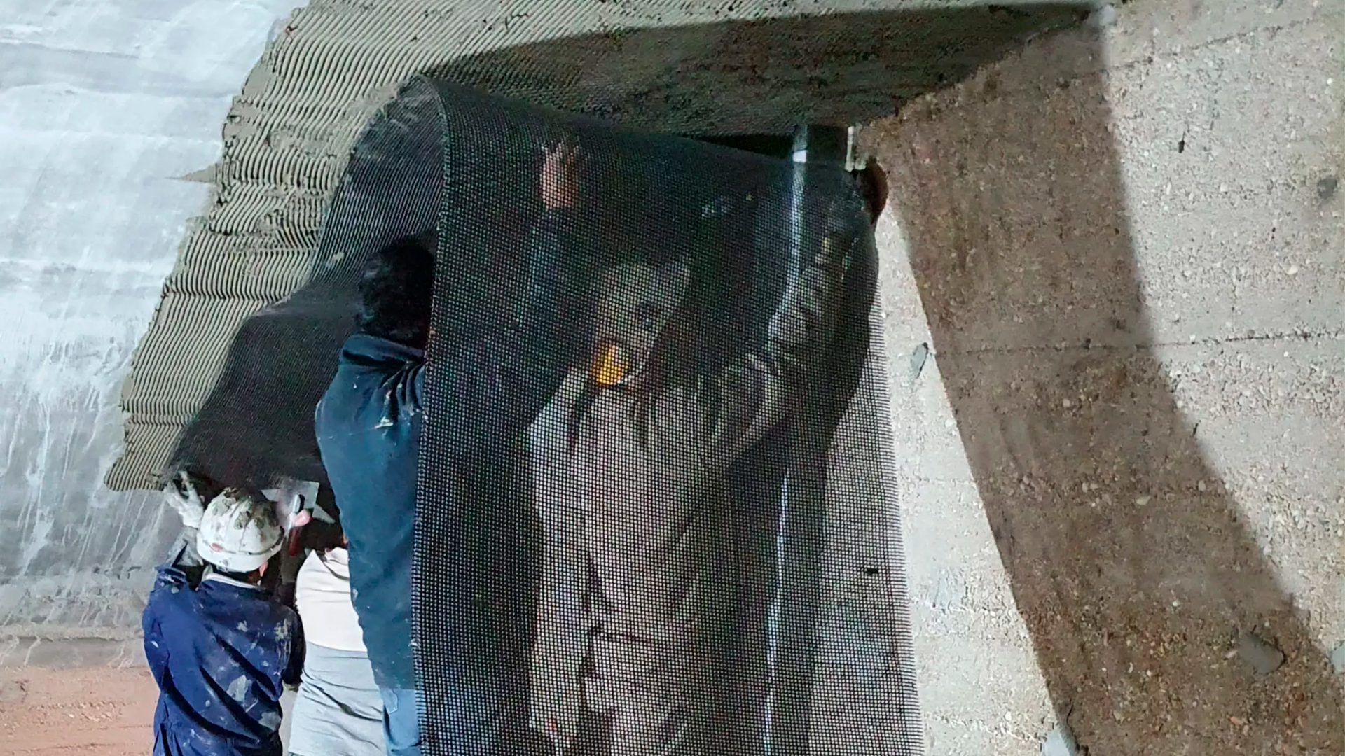 Construction workers installing mesh on concrete wall