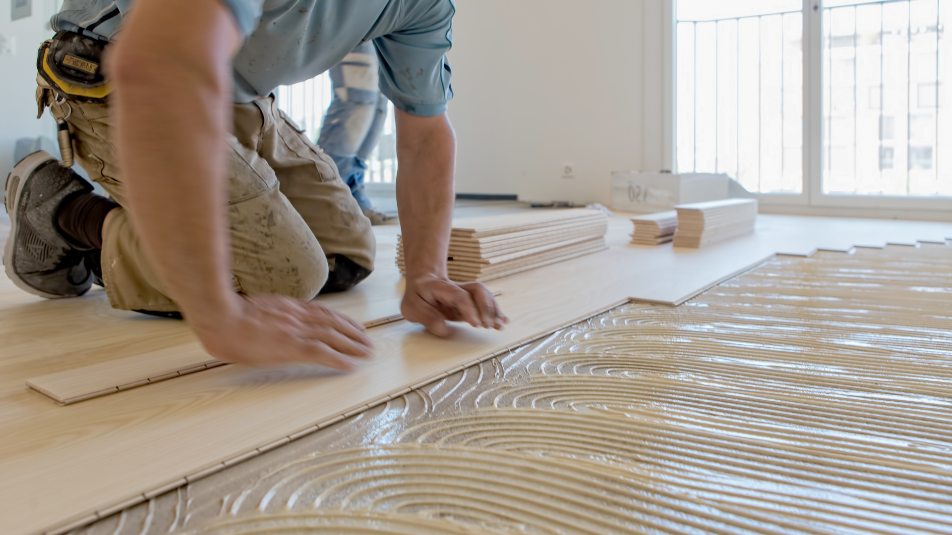 man applying wood panels over wood floor bonding adhesive