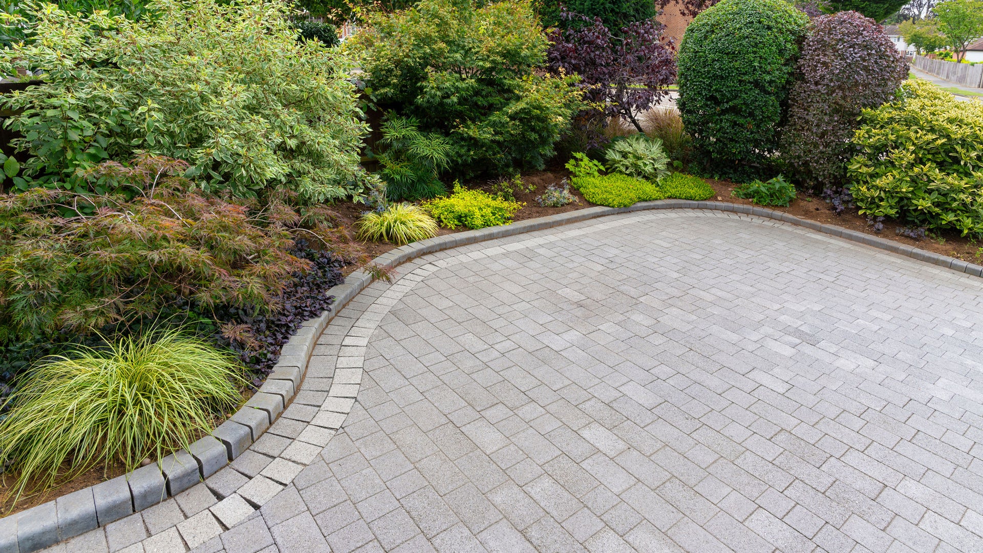 Stylish block paving drive with beautiful garden border with shrubs and flowers
