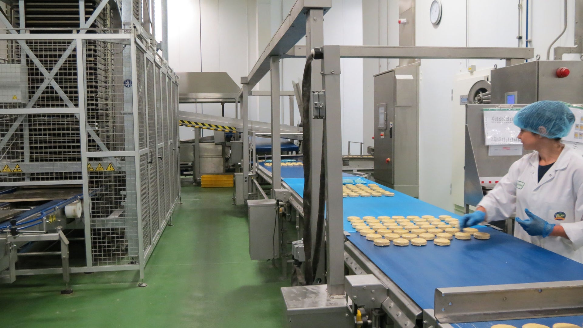 Industrial bakery production line with a worker in protective clothing inspecting and handling food items on a conveyor belt