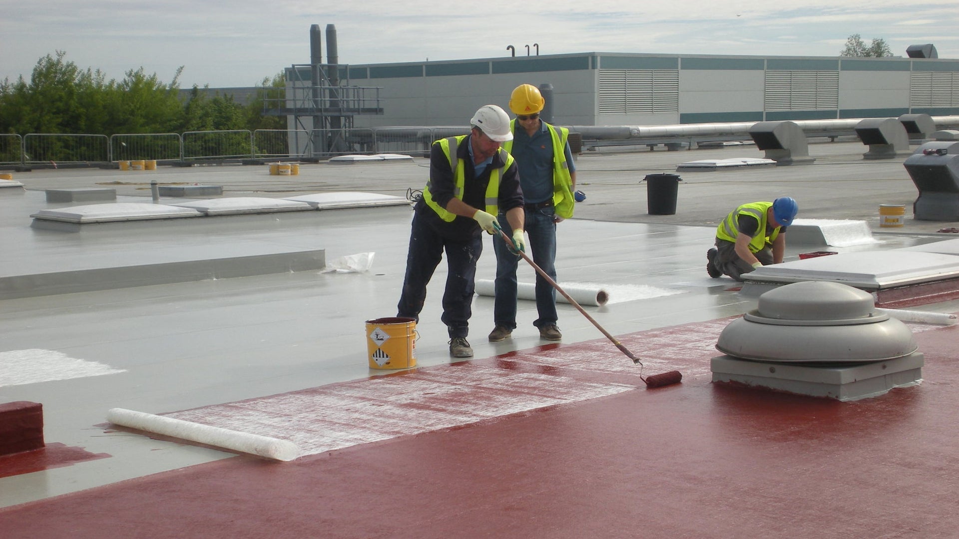 Construction workers applying coating on flat roof