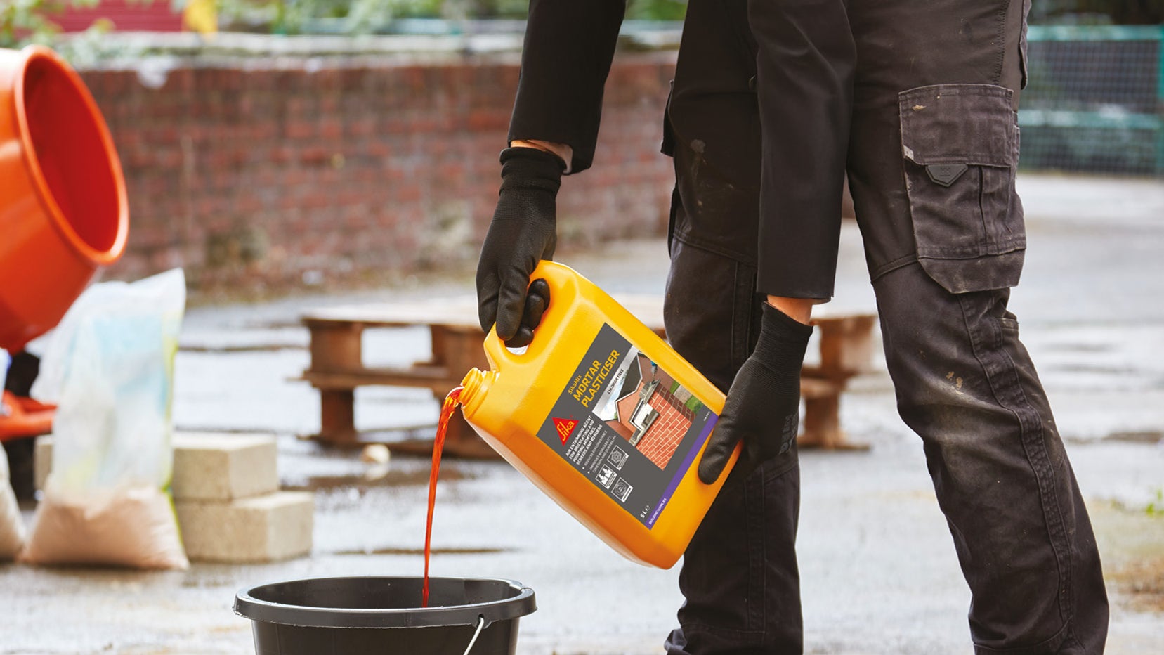 Worker pouring construction liquid into bucket