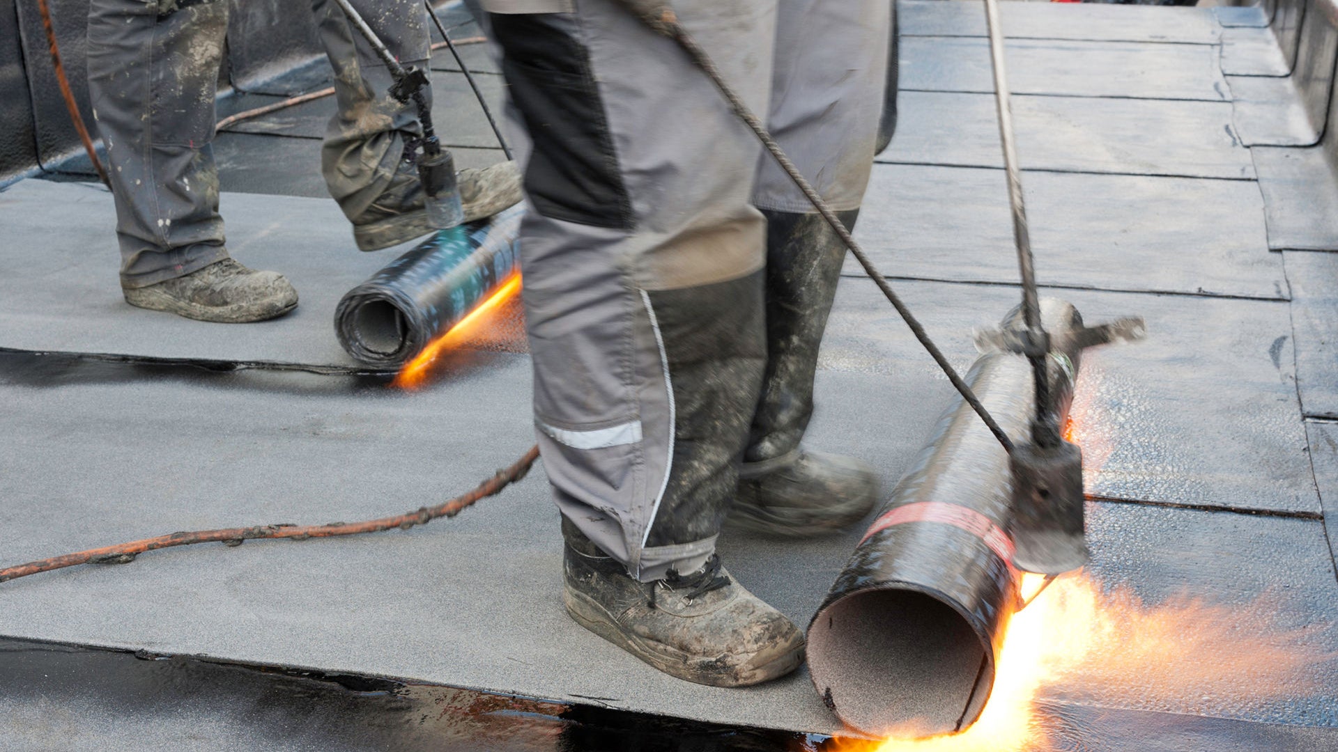 Foot rolling bitumen membrane and applying torch to adhere