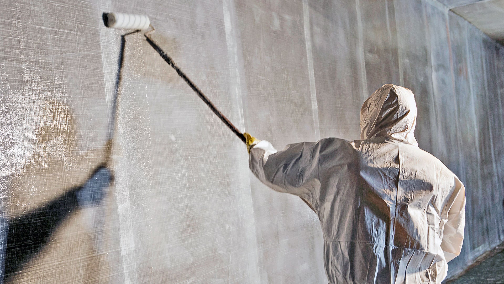 Worker painting wall with roller in protective suit