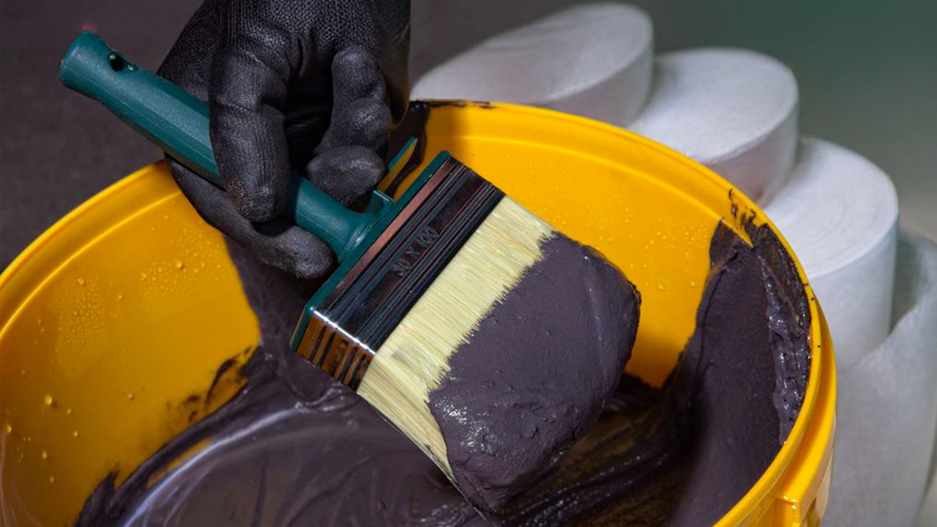 Gloved Hand Dipping Brush in Paint Bucket