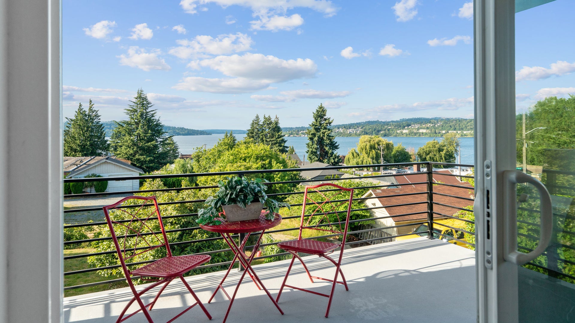 geöffnete Tür zu einem Balkon mit roten Gartenmöbel und einem wunderschönen Blick auf den See Washington
