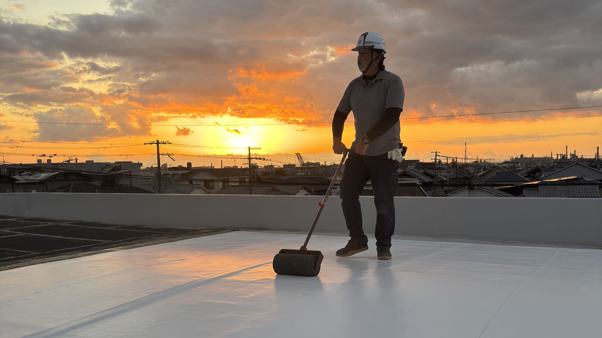 Worker Rolling Material on Rooftop at Sunset