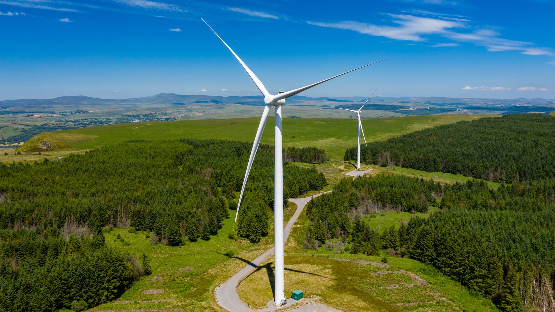 Aerial drone view of turbines at a large onshore windfarm on a green hillside (Pen y Cymoedd, Wales)
