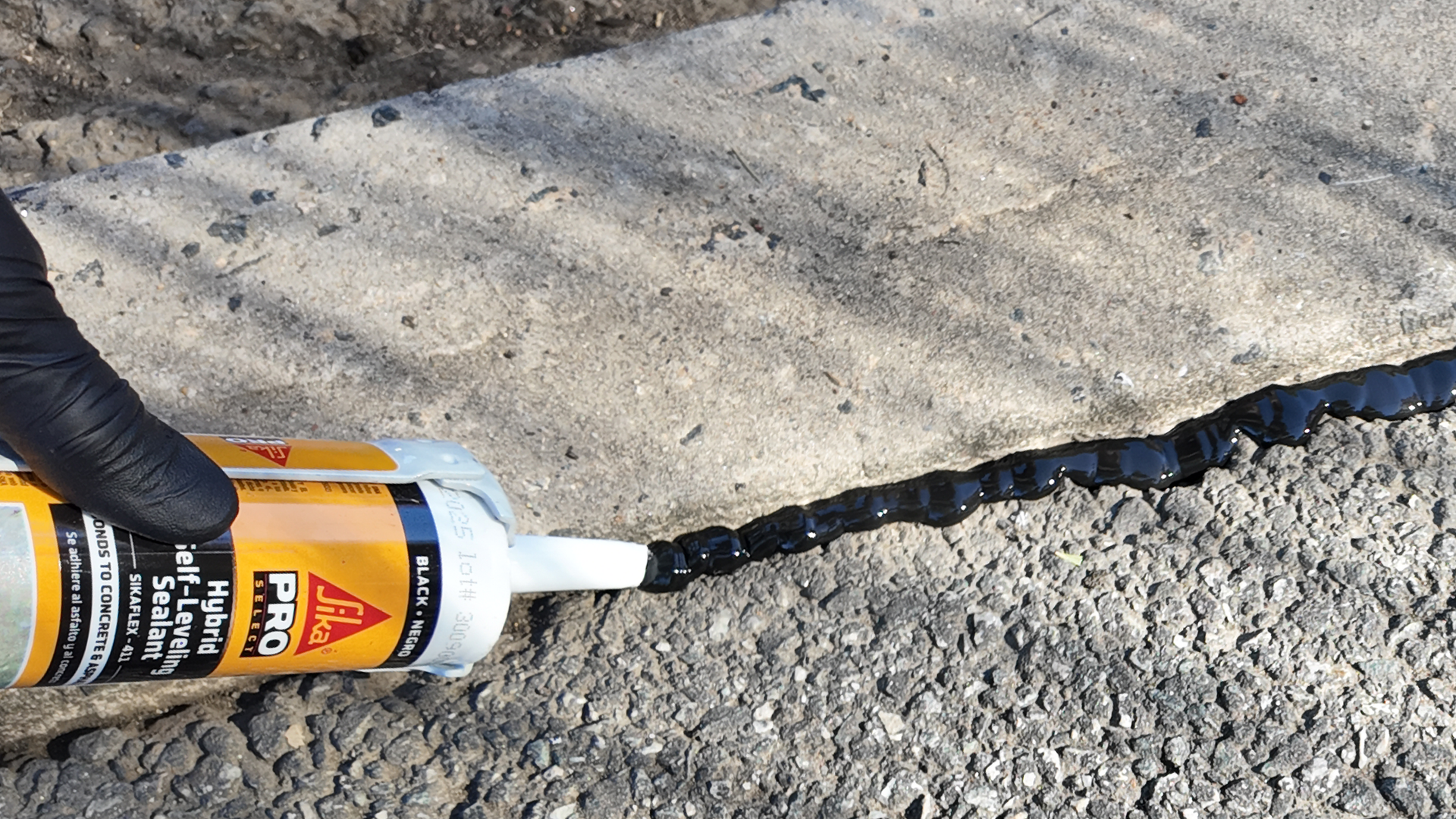 Applying asphalt sealant to concrete crack