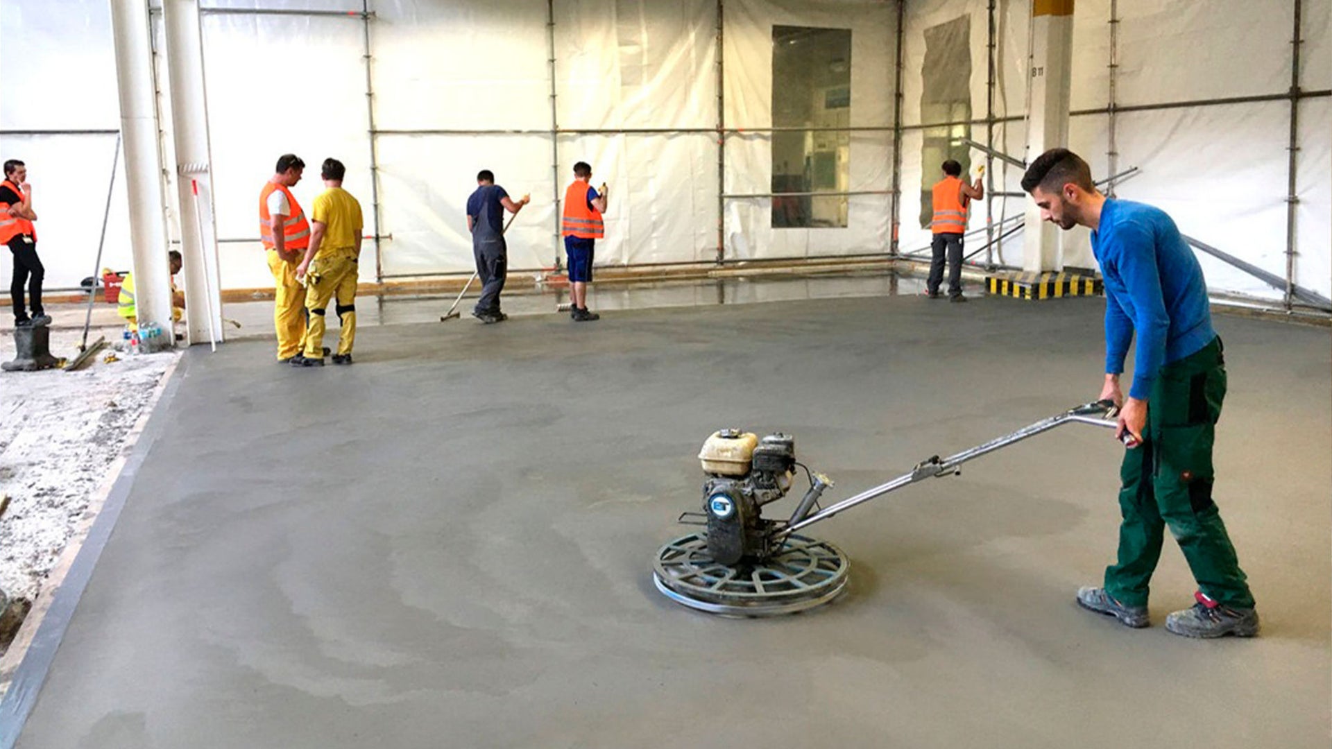 Construction workers smoothing concrete floor with machine