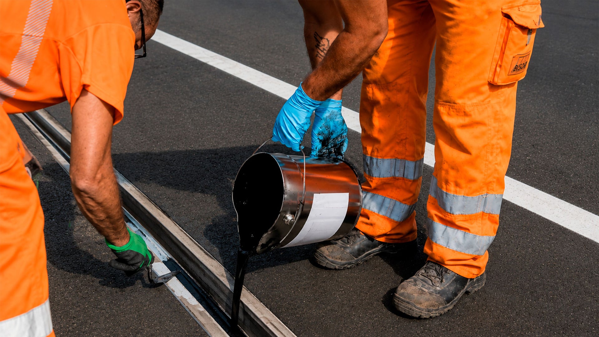 Road workers pouring sealant into pavement joint