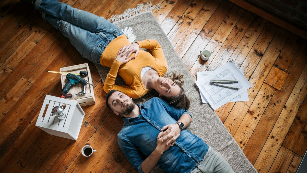 Young couple taking a break from painting and restoring their apartment by lying on the floor next to each other